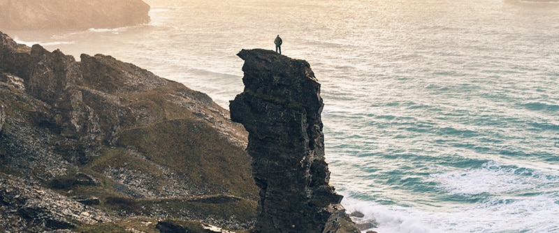 hiker at top of cliff by ocean - hypnosis for motivation and success