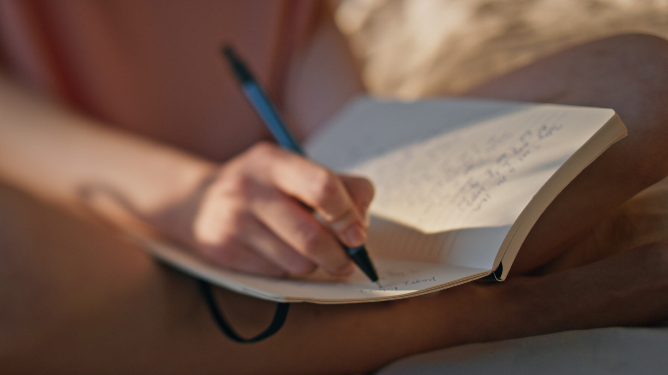 A close view of a hand writing in an open notebook in warm evening light.